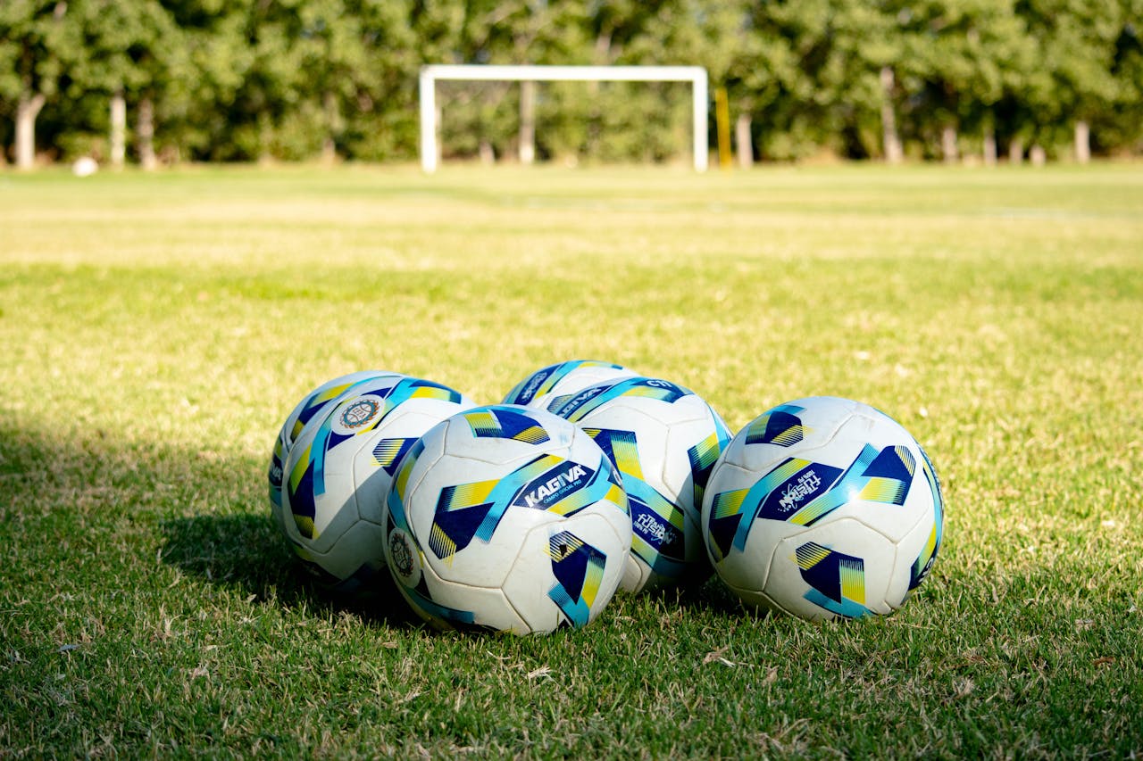 Five soccer balls rest on a green field, ready for a game in Mendoza, Argentina.